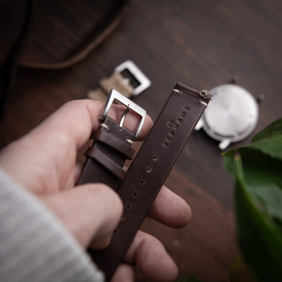 Hand holding a brown leather watch strap