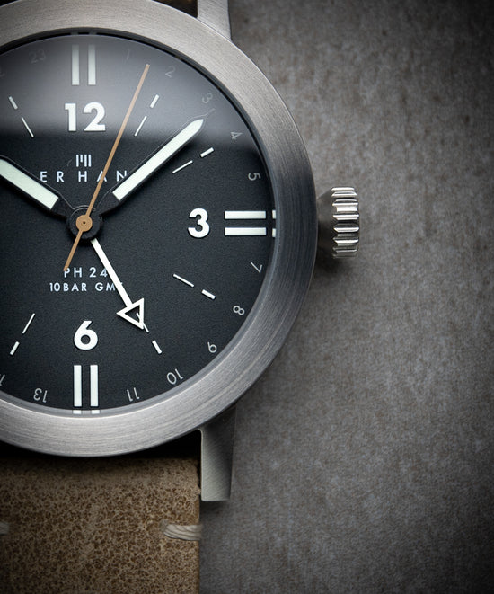 Close up on a watch with a black dial and a suede watch strap