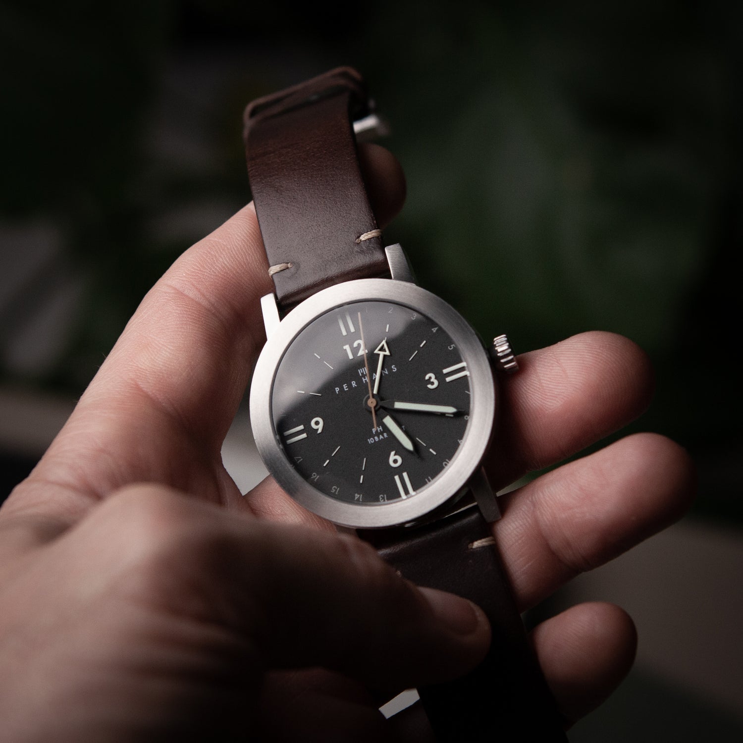 Hand holding a black dial watch with a brown leather strap